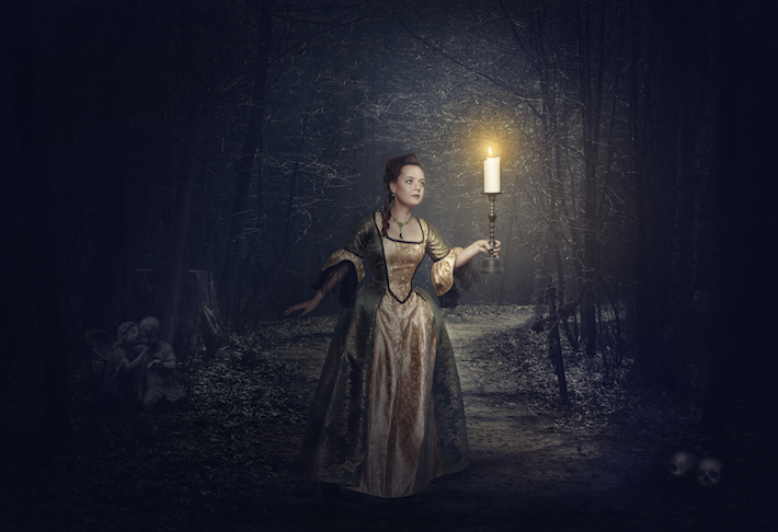 Beautiful woman with candle in medieval dress on the foggy road